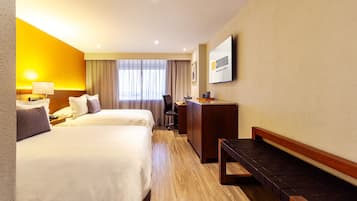 Una habitación de hotel con dos camas, un escritorio, una silla y un banco.