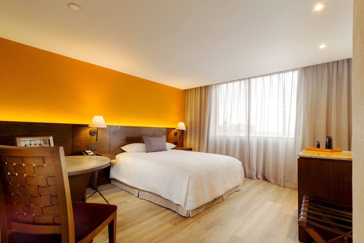 A hotel room with a bed, a desk, a chair, and a lamp.