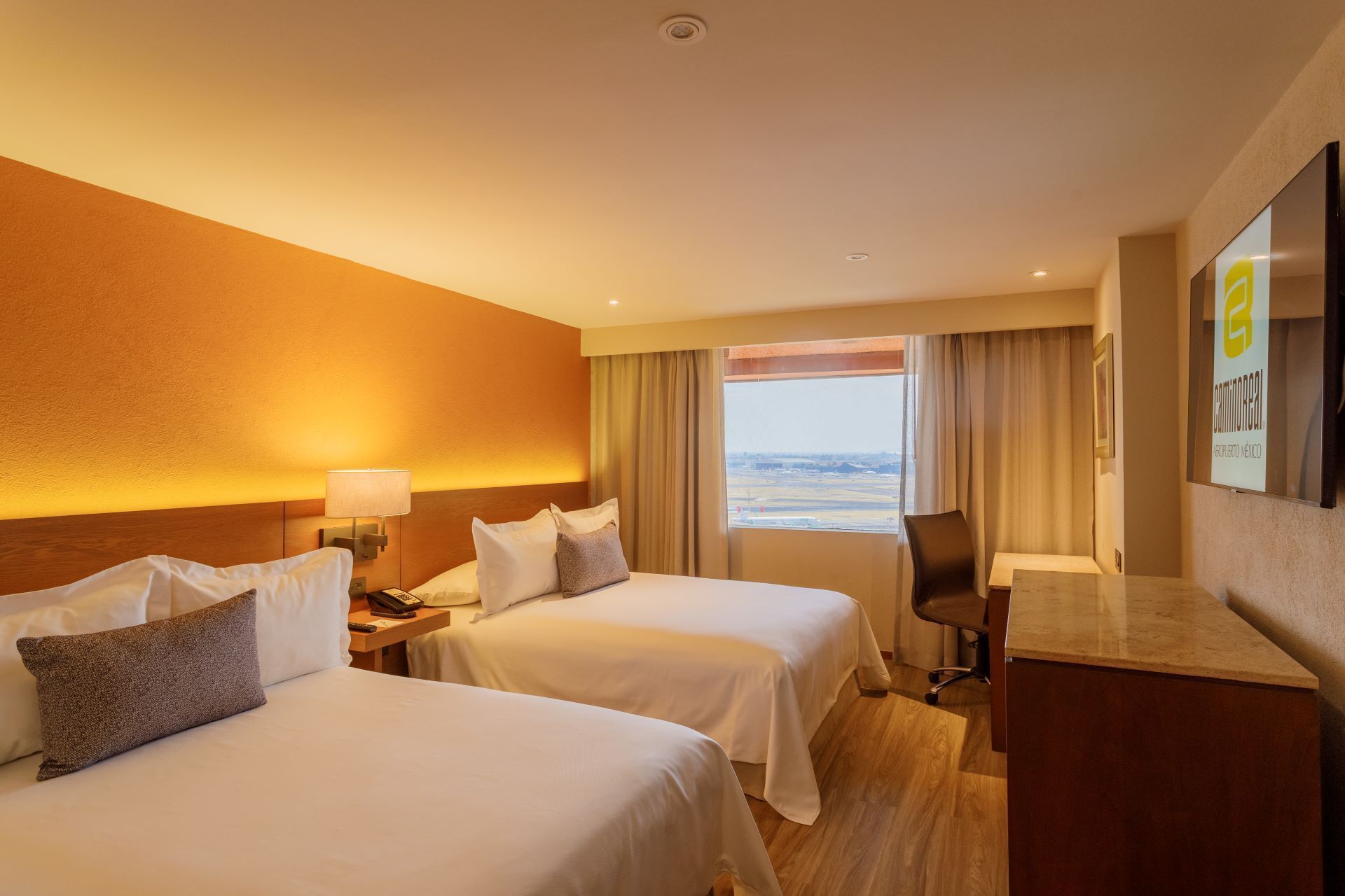 Habitación de hotel con dos camas, un escritorio, una silla, un televisor y vista al mar.