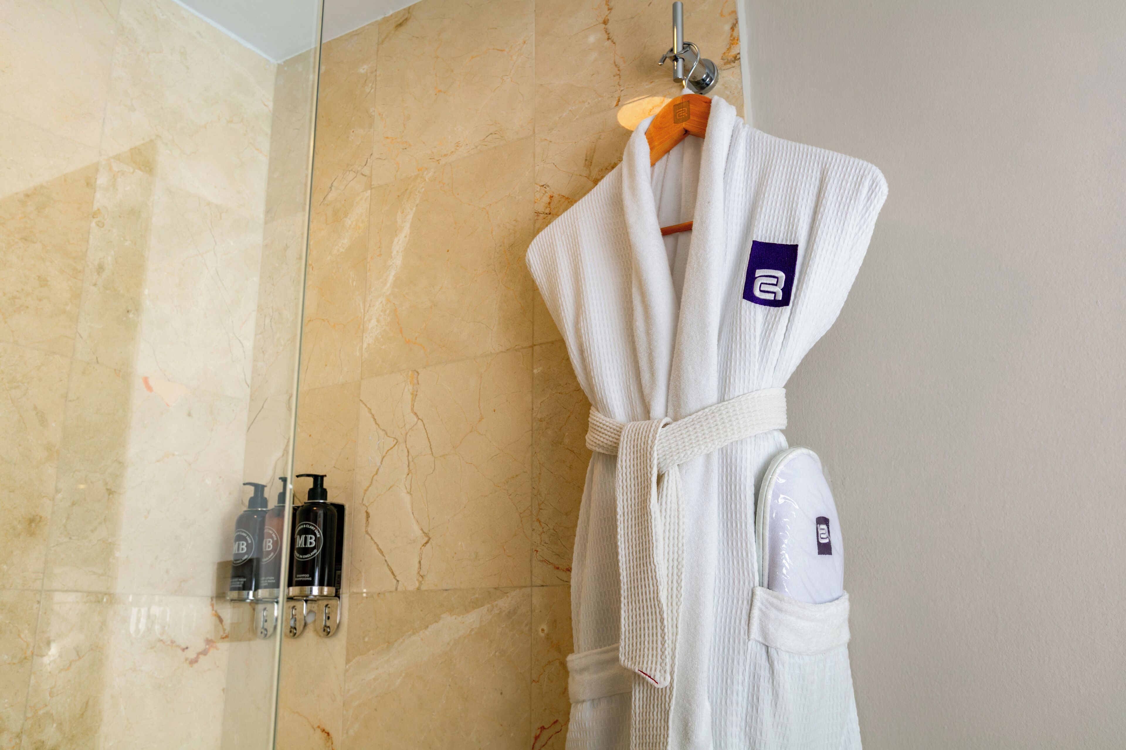 A bathroom with a marble wall, a white robe hanging on a rack, and toiletries on the wall.