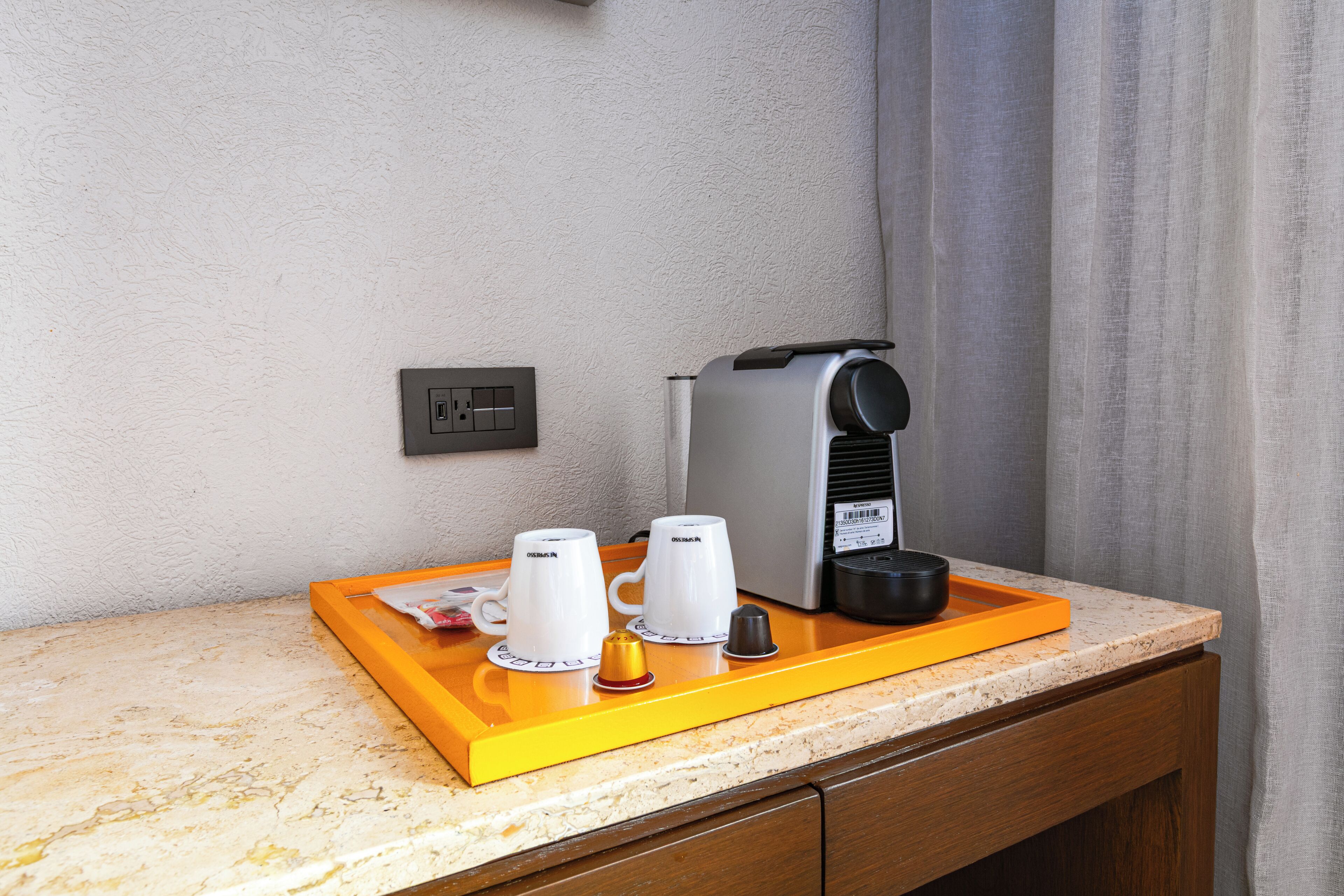 A coffee station with a coffee maker, two cups, and a tray on a countertop.