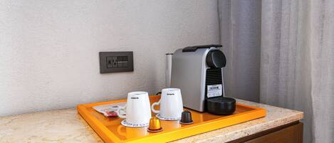 A coffee station with a coffee maker, two cups, and a tray on a countertop.