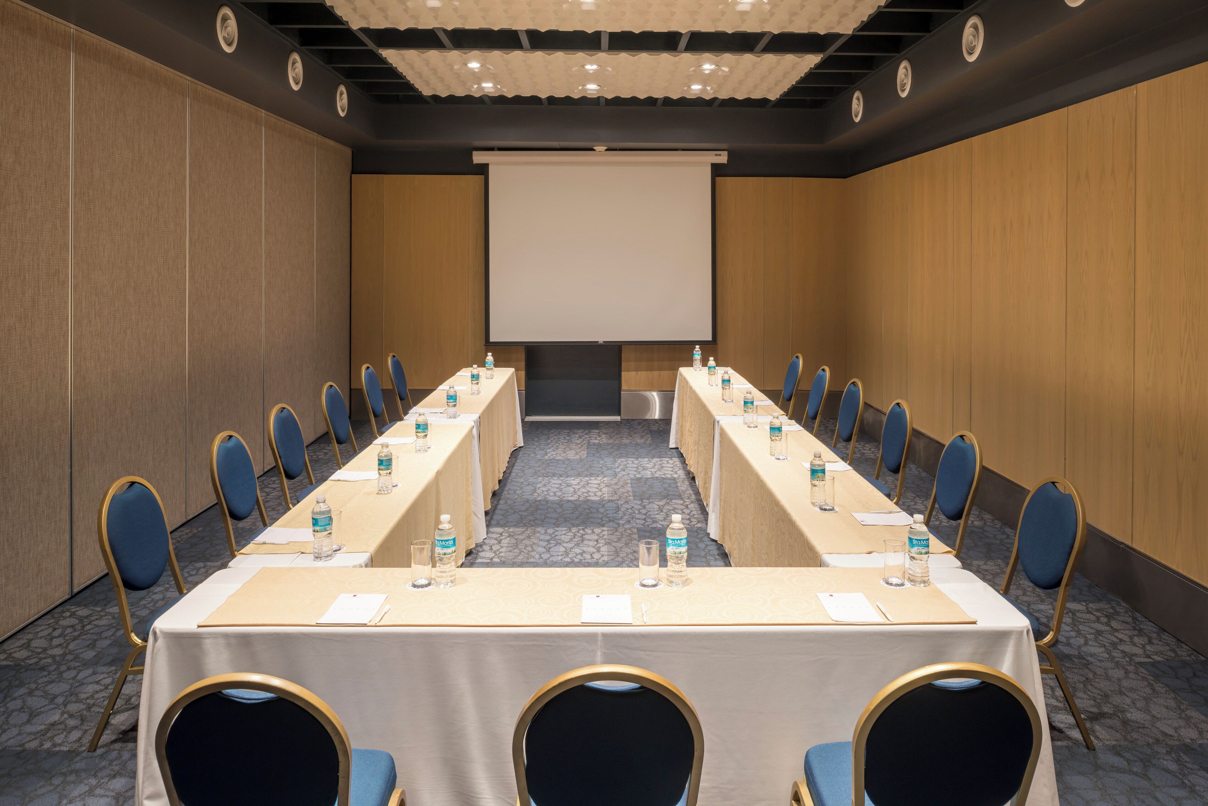 A conference room with a long table, chairs, a projector screen, and water bottles.