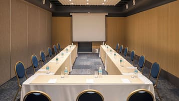 A conference room with a long table, chairs, a projector screen, and water bottles.