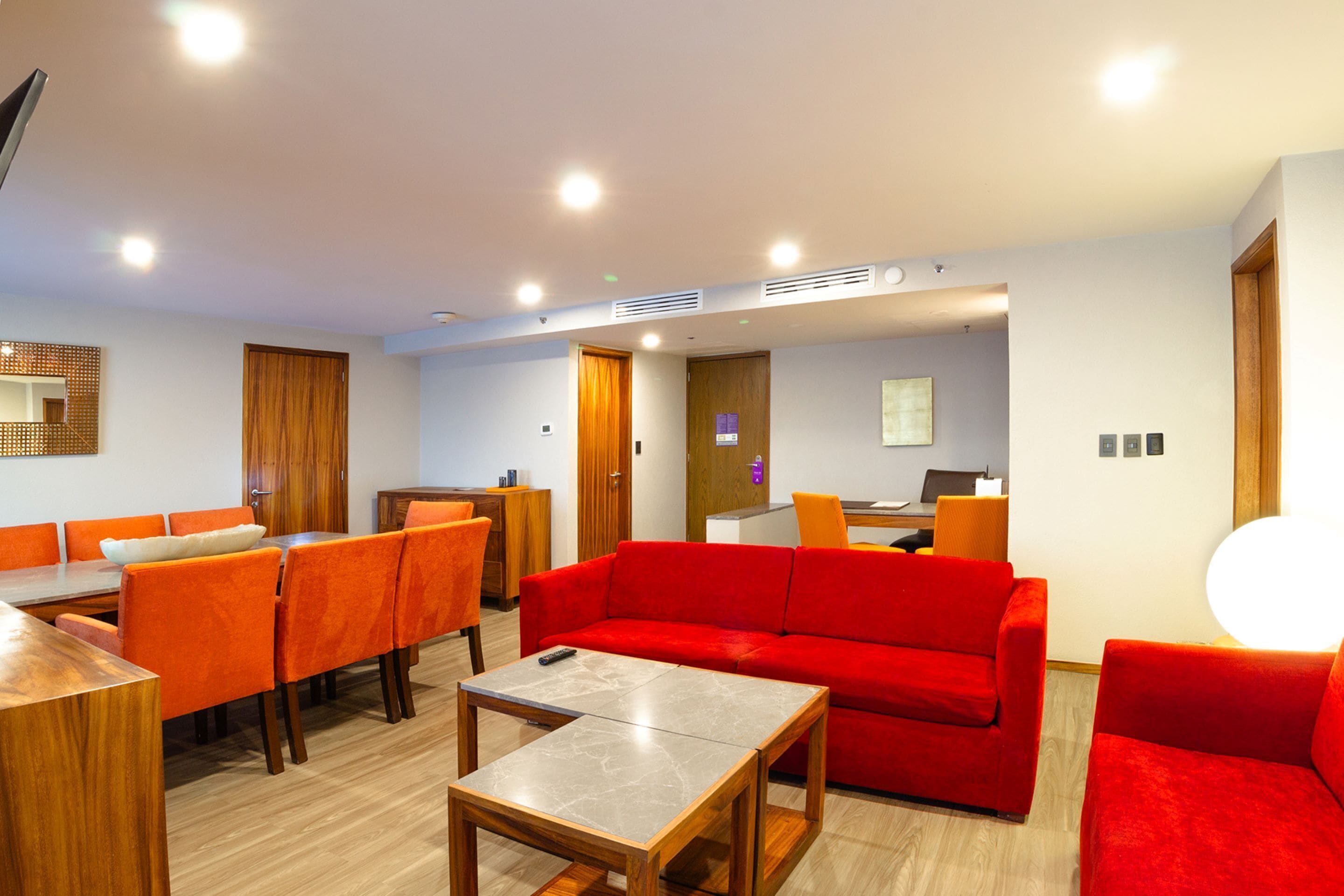 Ein modernes Hotelzimmer mit Essbereich, einem roten Sofa und einem Holzesstisch.