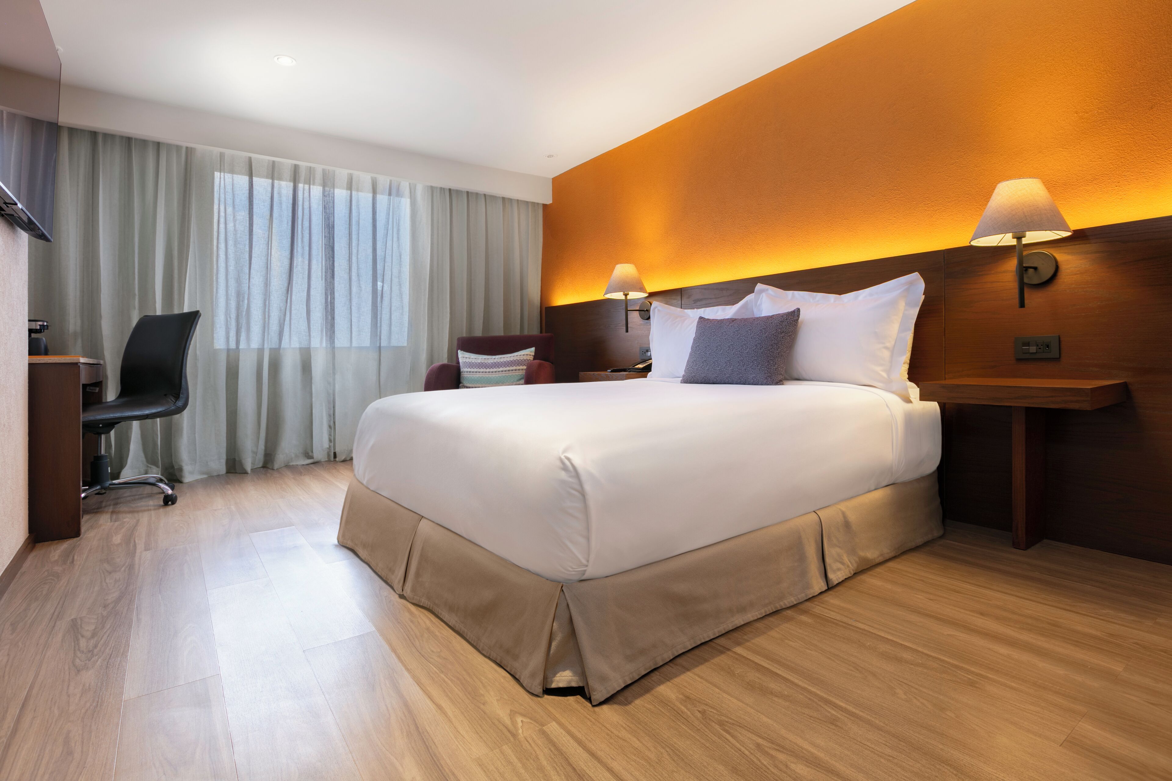 Una habitación de hotel moderna con una cama grande, un escritorio, una silla y una ventana con cortinas.