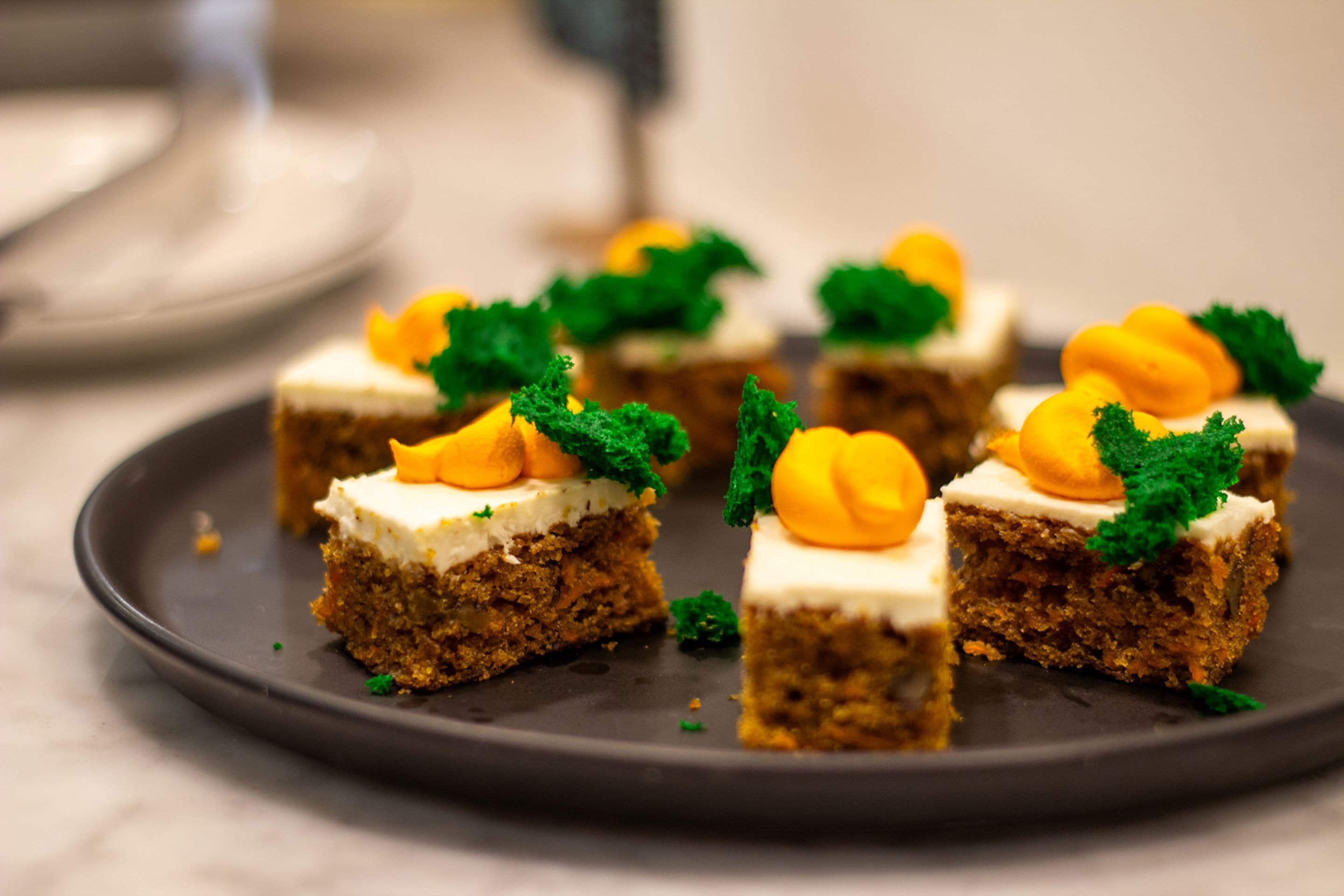 Un piatto con diversi dolcetti quadrati, guarniti da foglie verdi e decorazioni gialle.