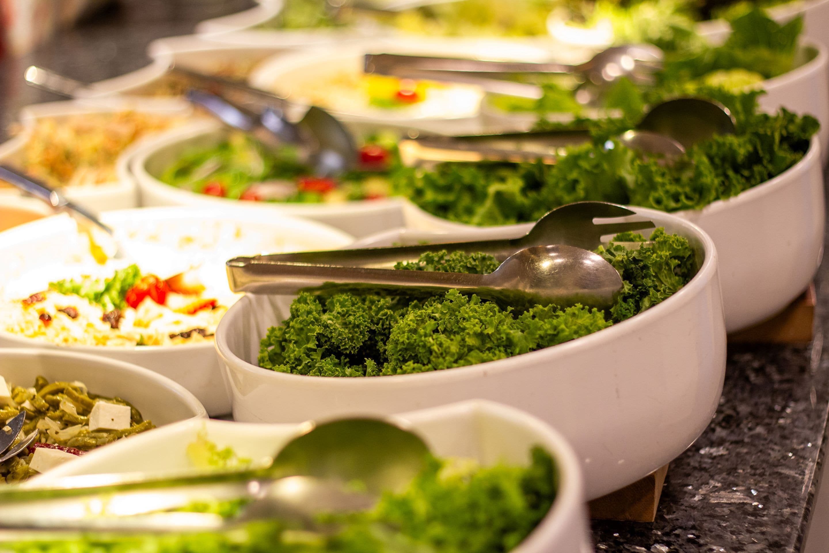 A buffet with various dishes, including a prominent bowl of green salad.