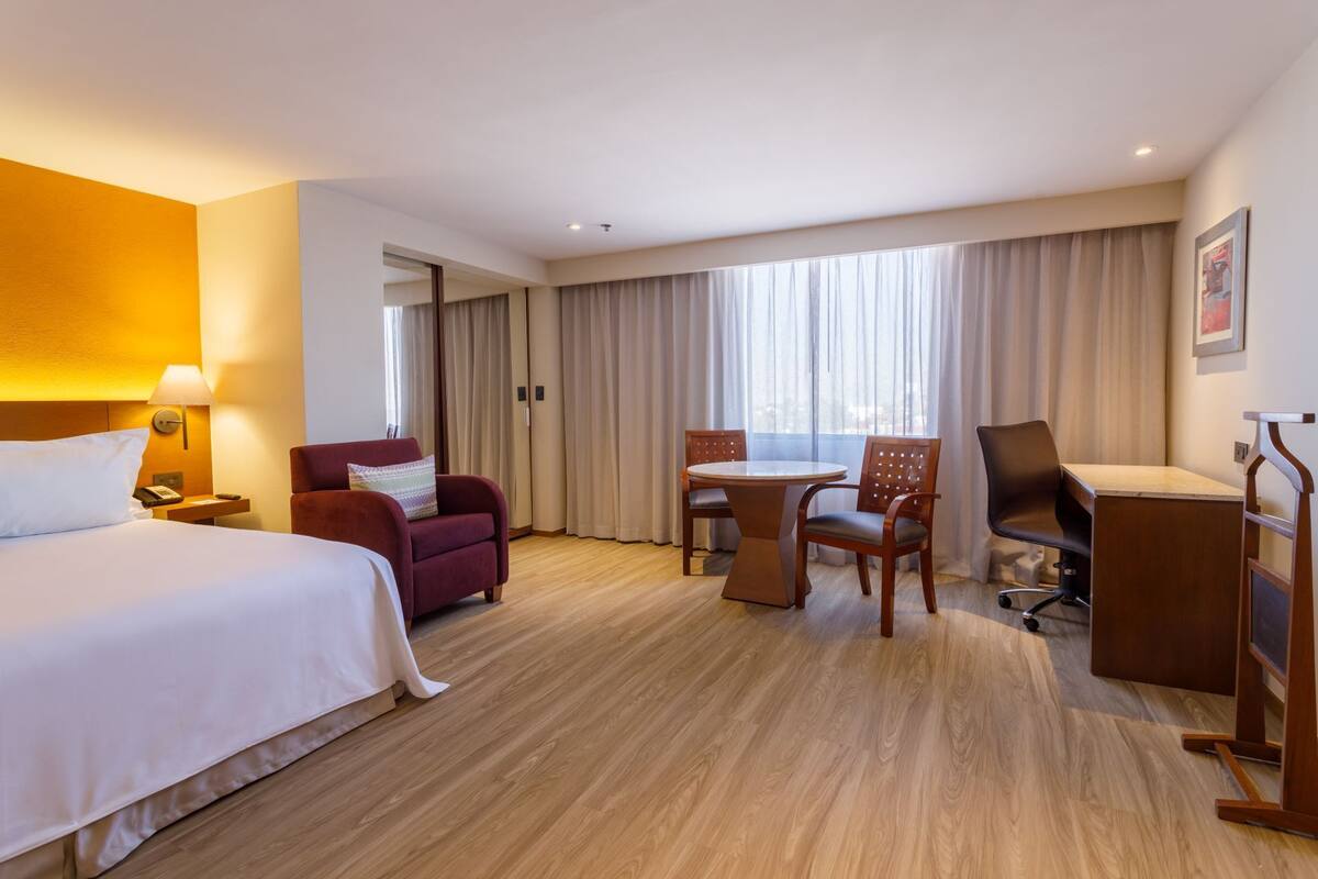 A hotel room with a bed, a desk, a chair, a sofa, and a dining table.