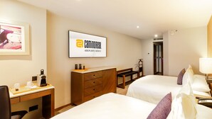 A hotel room with two beds, a desk with a coffee maker, a dresser, and a framed sign on the wall. - Camino Real Aeropuerto Mexico (Mexico City)