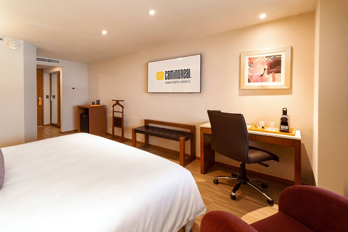 A hotel room with a bed, desk, chair, and a framed picture on the wall.