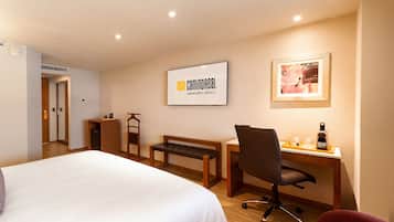 Una habitación de hotel con cama, escritorio, silla y un cuadro en la pared.