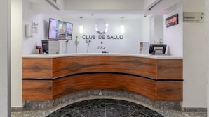 A reception desk with a wooden finish, a digital clock, and a sign for the Club de Salud & SPA. - Camino Real Aeropuerto Mexico (Mexico City)