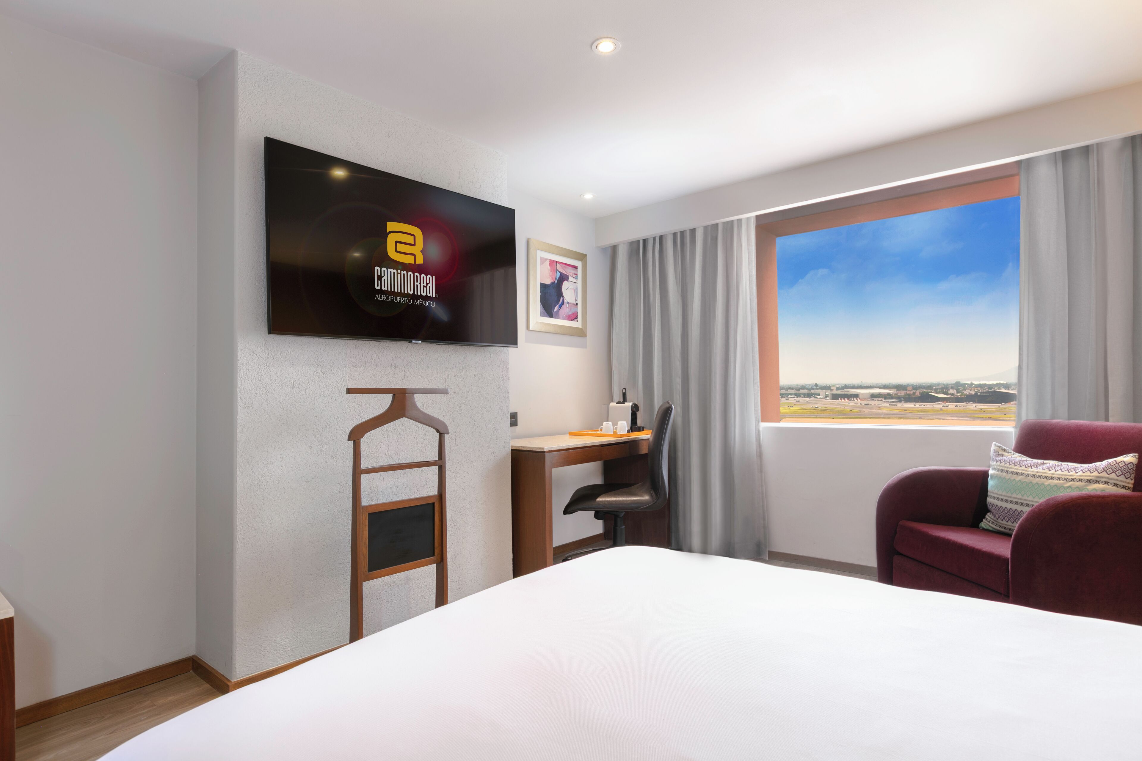 Habitación de hotel con cama, escritorio, silla, televisor montado en la pared y ventana con vistas.