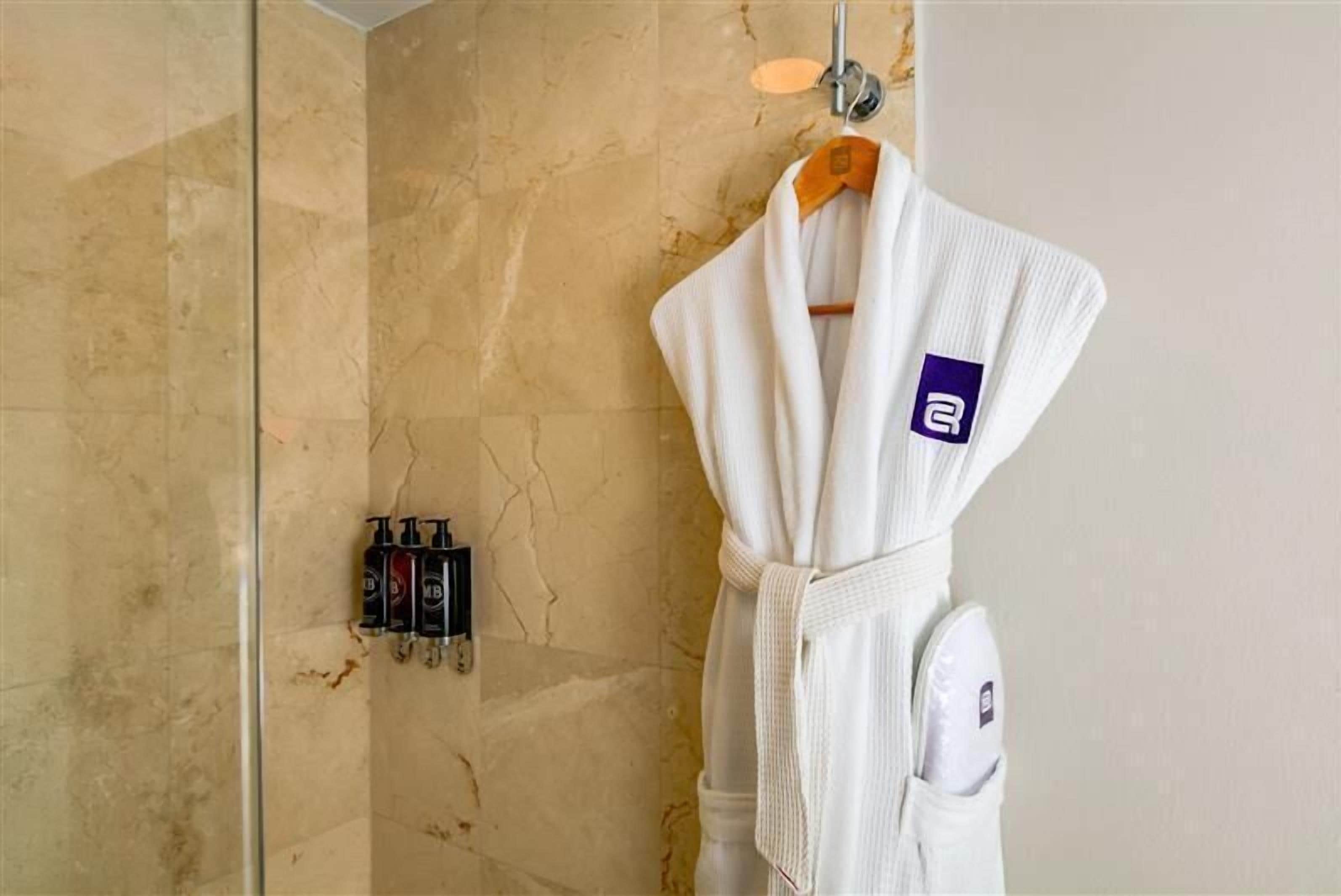 Un baño con pared de mármol, una bata blanca colgada en un perchero y una zona de ducha.