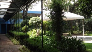 A covered walkway with a glass ceiling, surrounded by lush greenery and a white canopy tent.