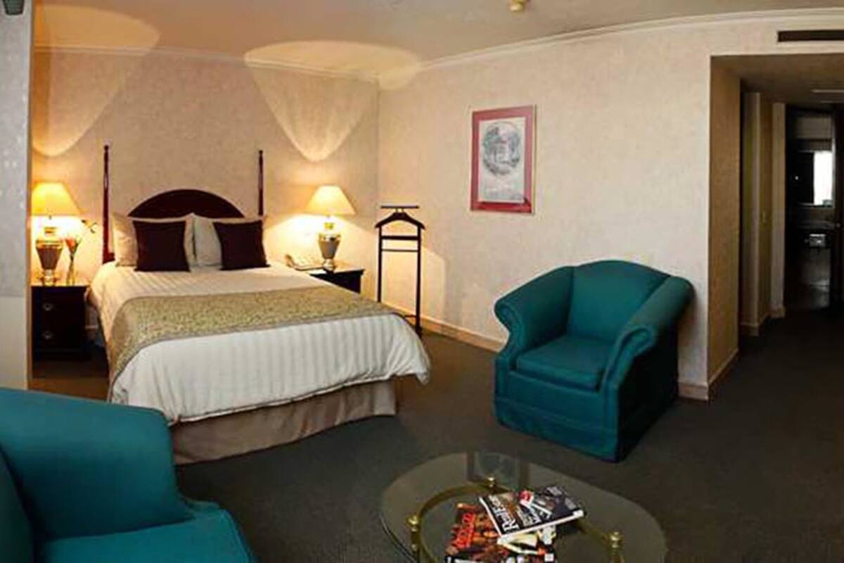 Hotellihuone, jossa on sänky, kaksi tuolia, yöpöytä ja lamppu.