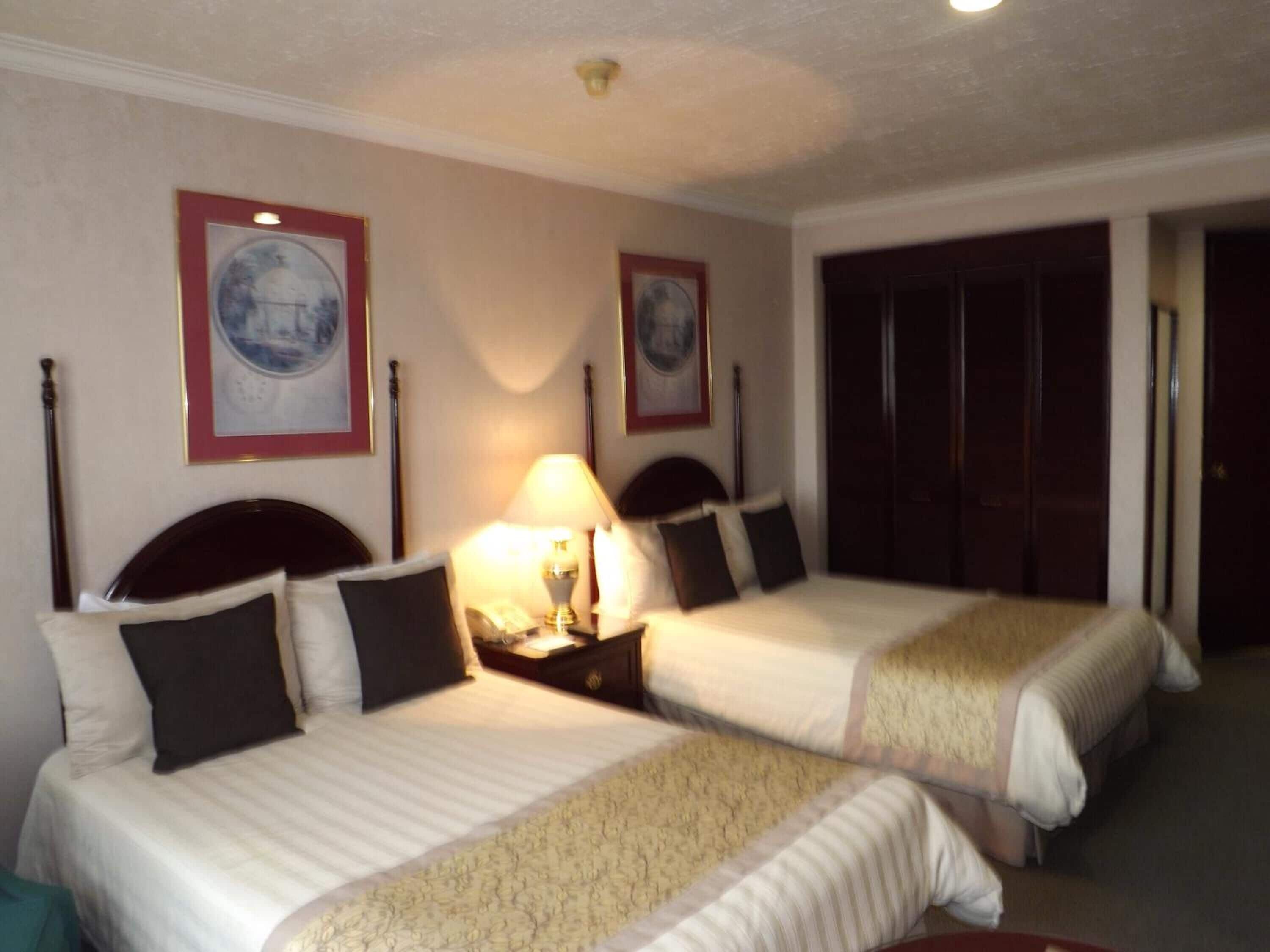Habitación de hotel con dos camas, una mesita de noche con lámpara y un armario.