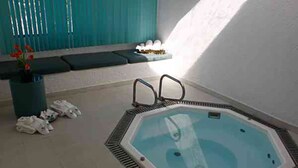 A hexagonal hot tub with a metal frame, a potted plant with red flowers, and a bench with a cushion.