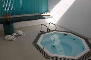 Un bain à remous hexagonal doté d’une structure métallique, une plante en pot aux fleurs rouges et un banc avec un coussin.