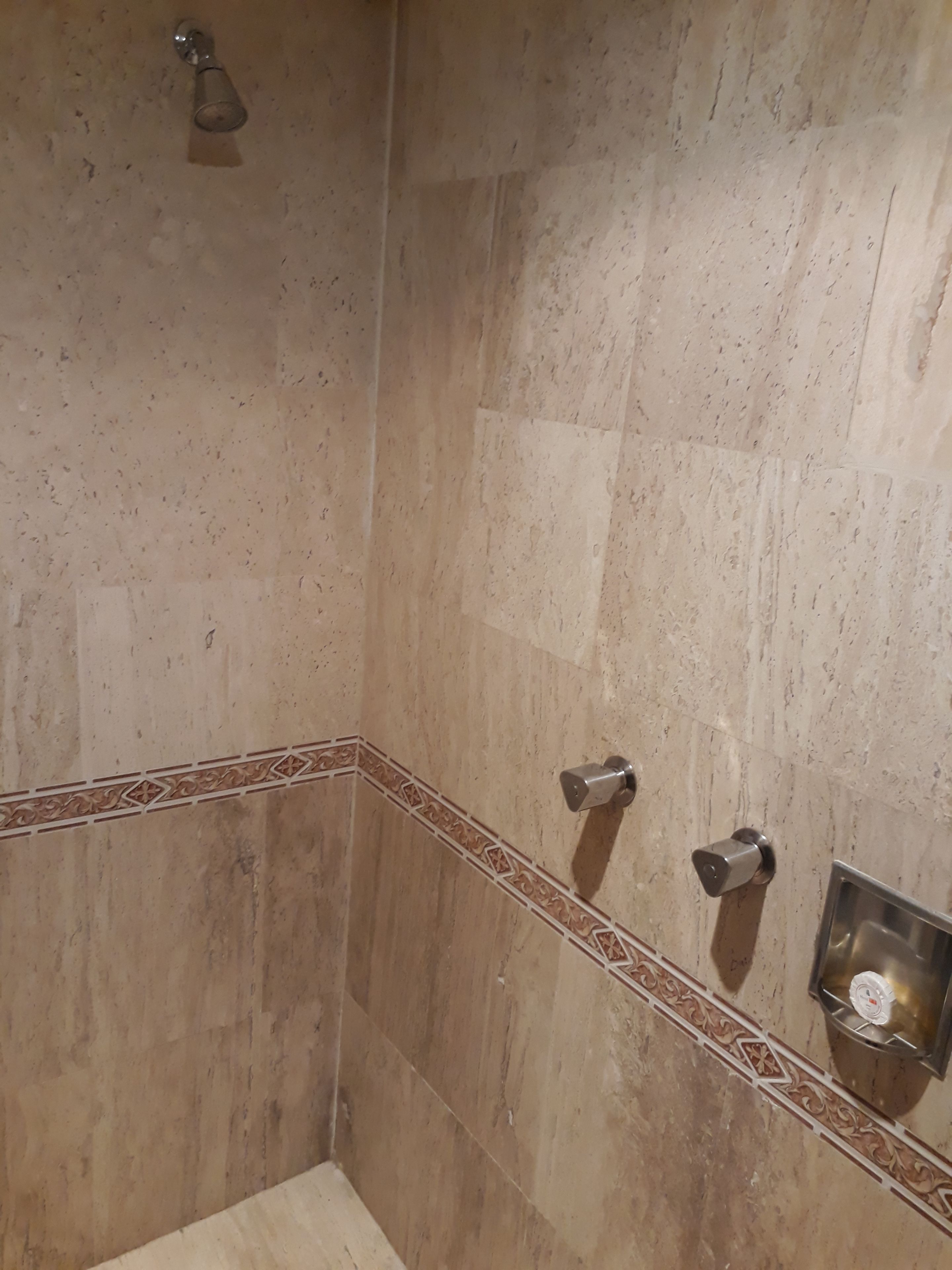 Un baño con paredes de azulejos color beige, zona de ducha y lavabo en esquina con grifo.