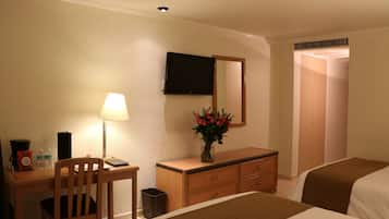 Habitación de hotel con cama, escritorio con lámpara, cómoda, televisor montado en la pared y espejo.
