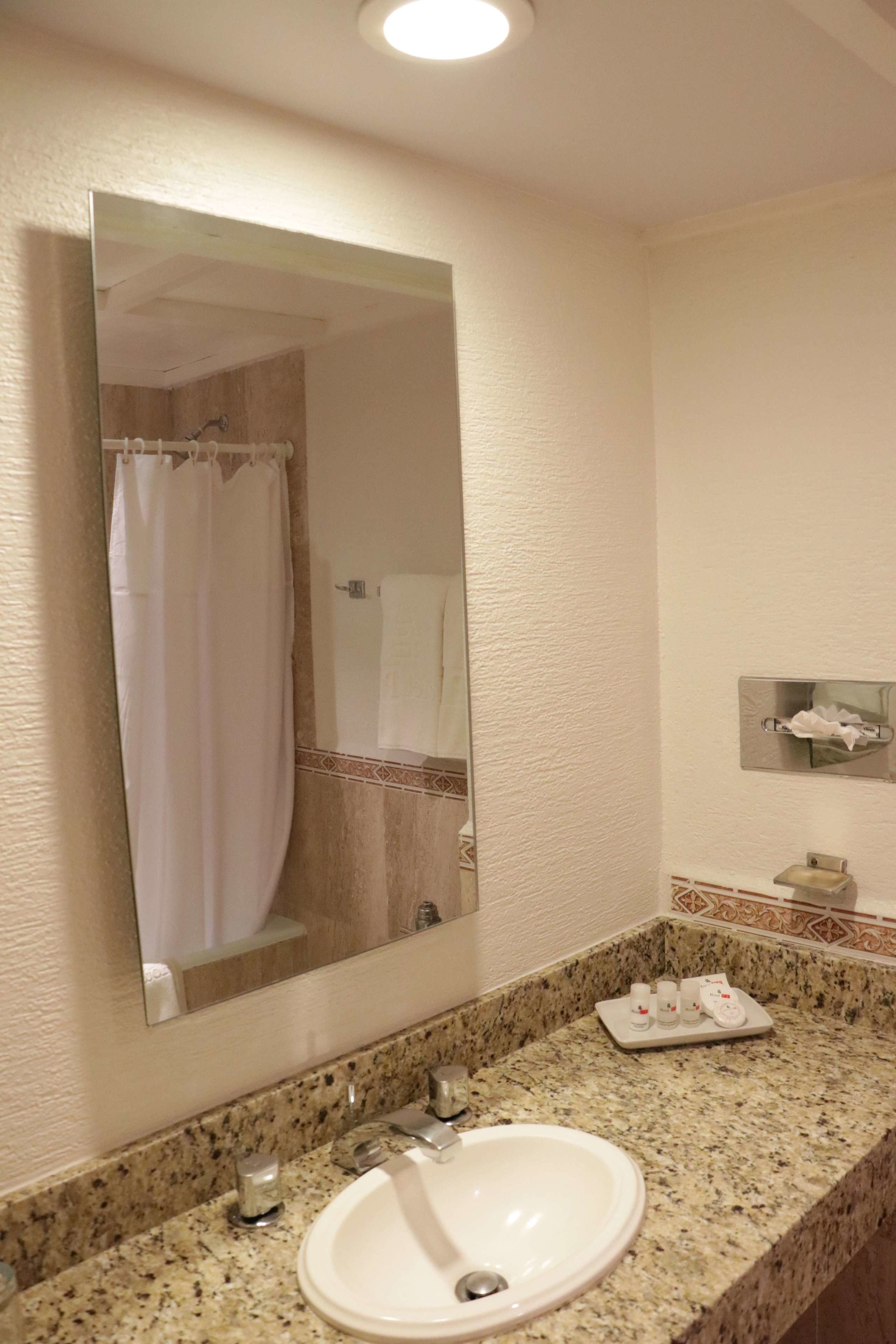 Un baño con encimera de granito, un lavabo, un espejo y cortina de ducha.