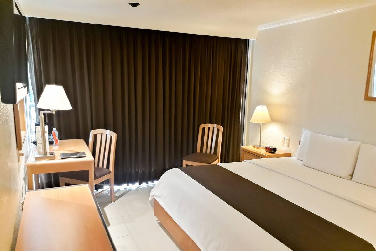 Ett hotellrum med en säng, två stolar, ett skrivbord, en lampa och ett nattduksbord.