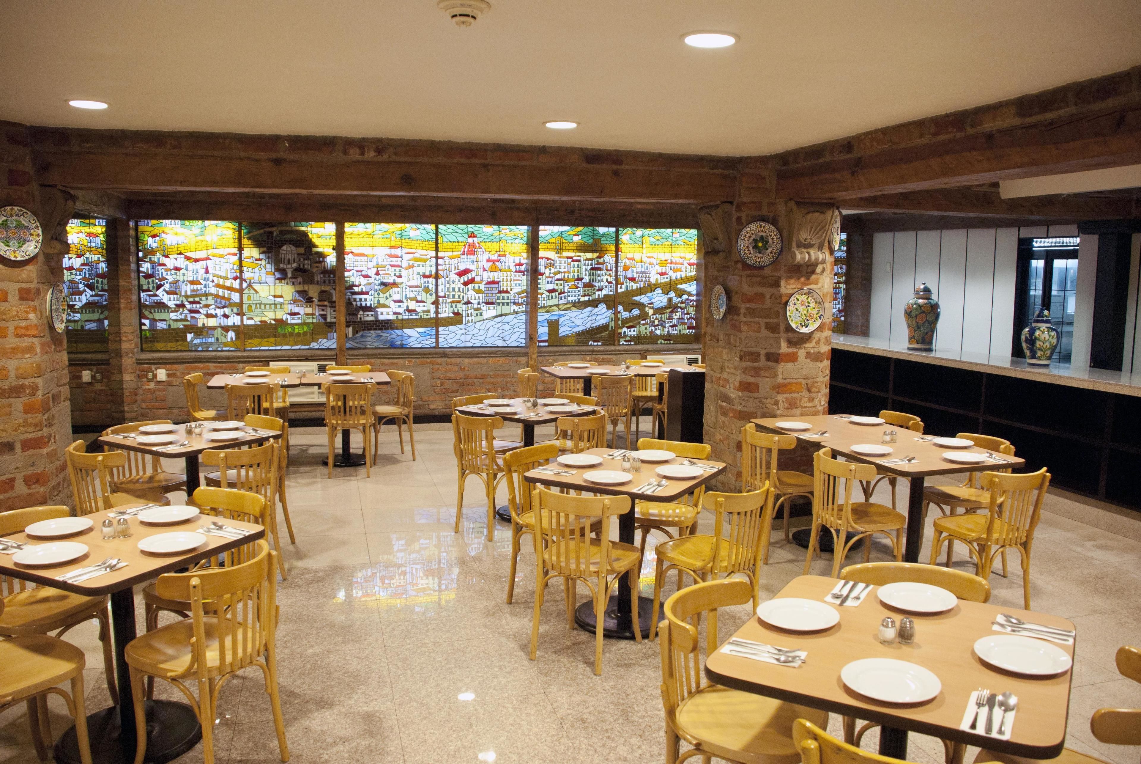 A restaurant with brick walls, large windows with a city view, and wooden tables and chairs.