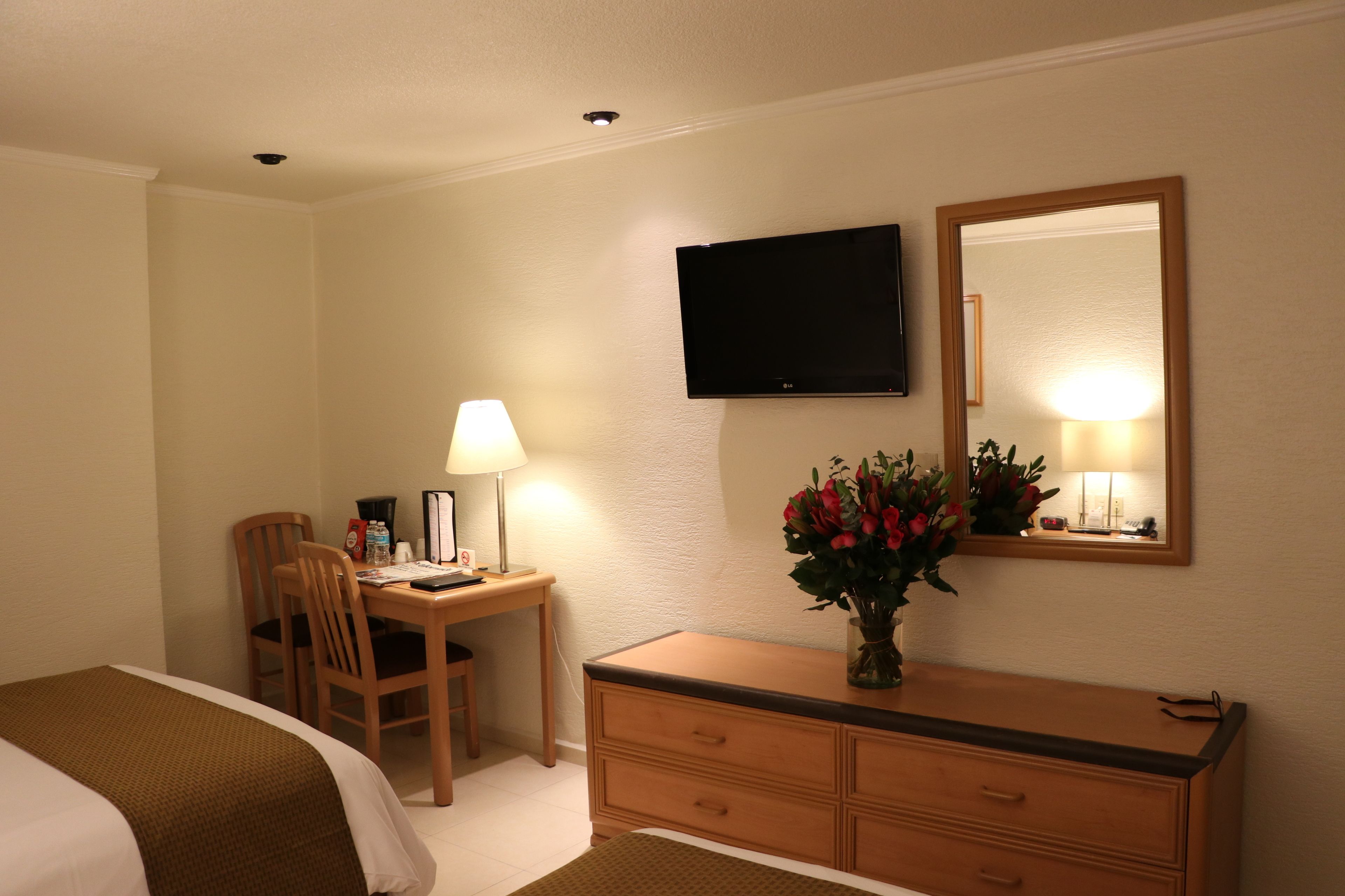 A hotel room with a bed, a desk with a chair, a dresser, a TV, and a mirror.