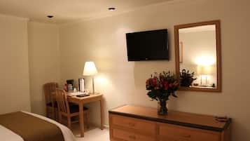Una habitación de hotel con cama, escritorio con silla, cómoda, televisor y espejo.