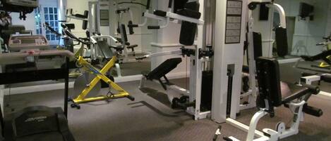 A gym with various exercise machines, mirrors, and a television.