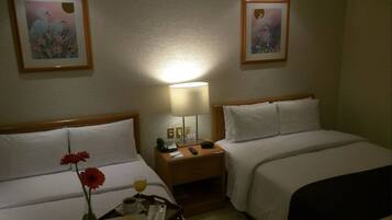 Une chambre d’hôtel avec deux lits, une table de chevet avec une lampe, un plateau avec des articles pour le petit-déjeuner et deux tableaux encadrés au mur.