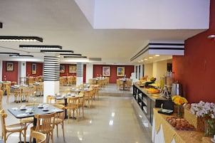 Un grand espace dédié à la salle à manger, avec plusieurs tables et chaises, un buffet proposant une variété de plats et des œuvres d’art accrochées aux murs.
