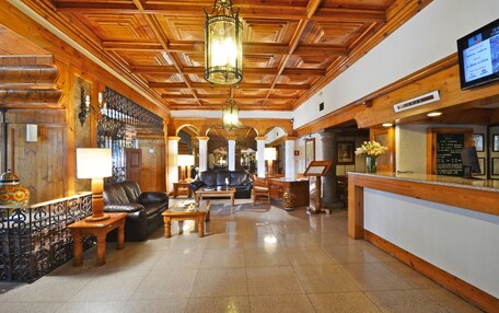 A lobby with wooden paneling, a reception desk, leather seating, and a chandelier.