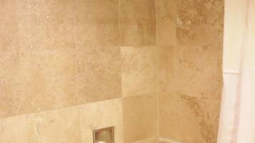 Una ducha con azulejos color beige, una cortina de ducha blanca y un cabezal de ducha de mano.