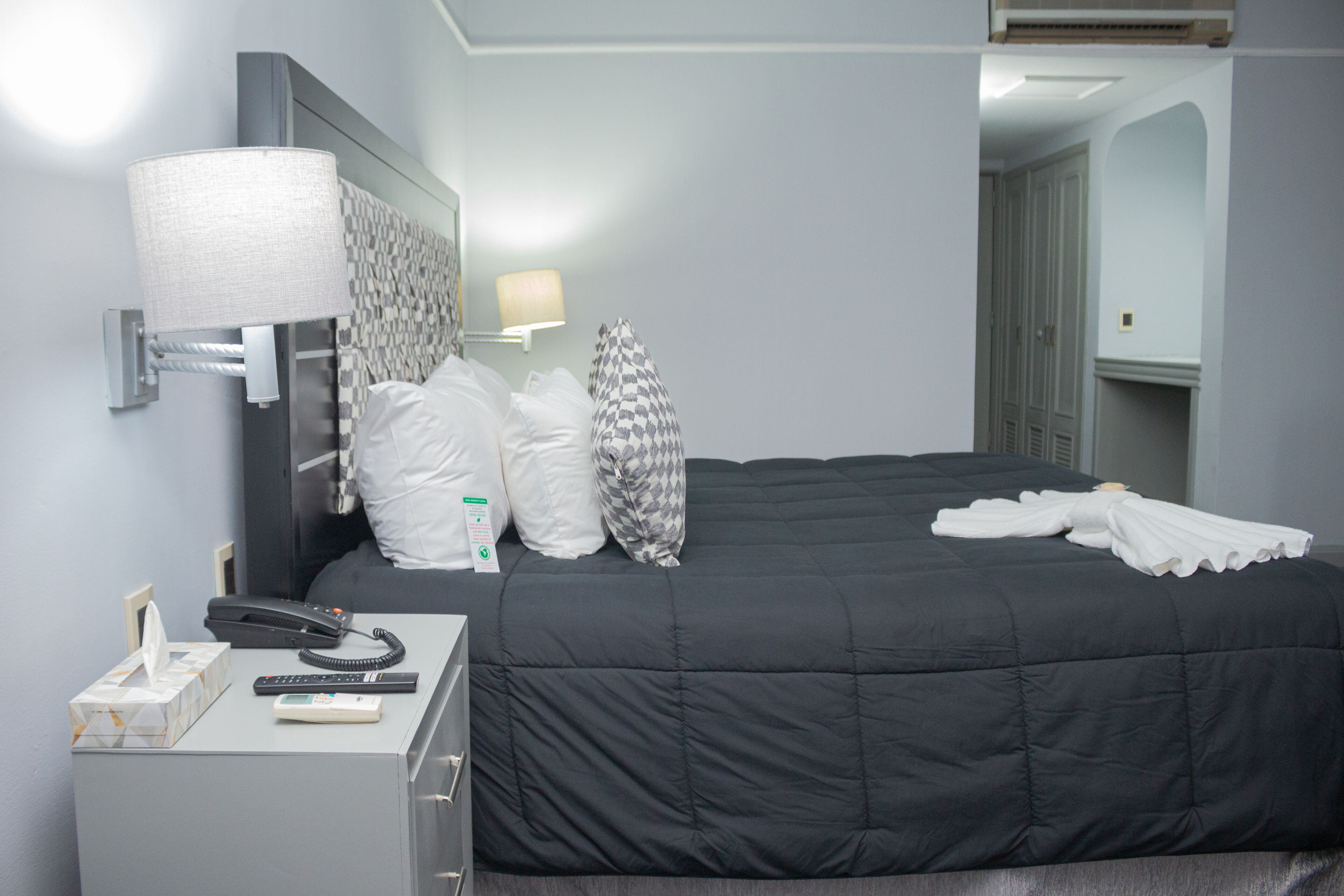Ein Hotelzimmer mit einem Bett, einem Nachttisch mit Lampe, einem Telefon und einer Taschentuchbox.