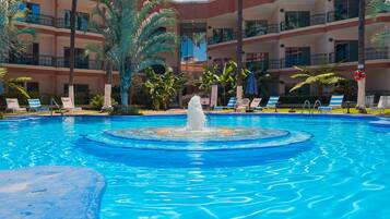Una piscina con una fuente central, rodeada de tumbonas y palmeras.