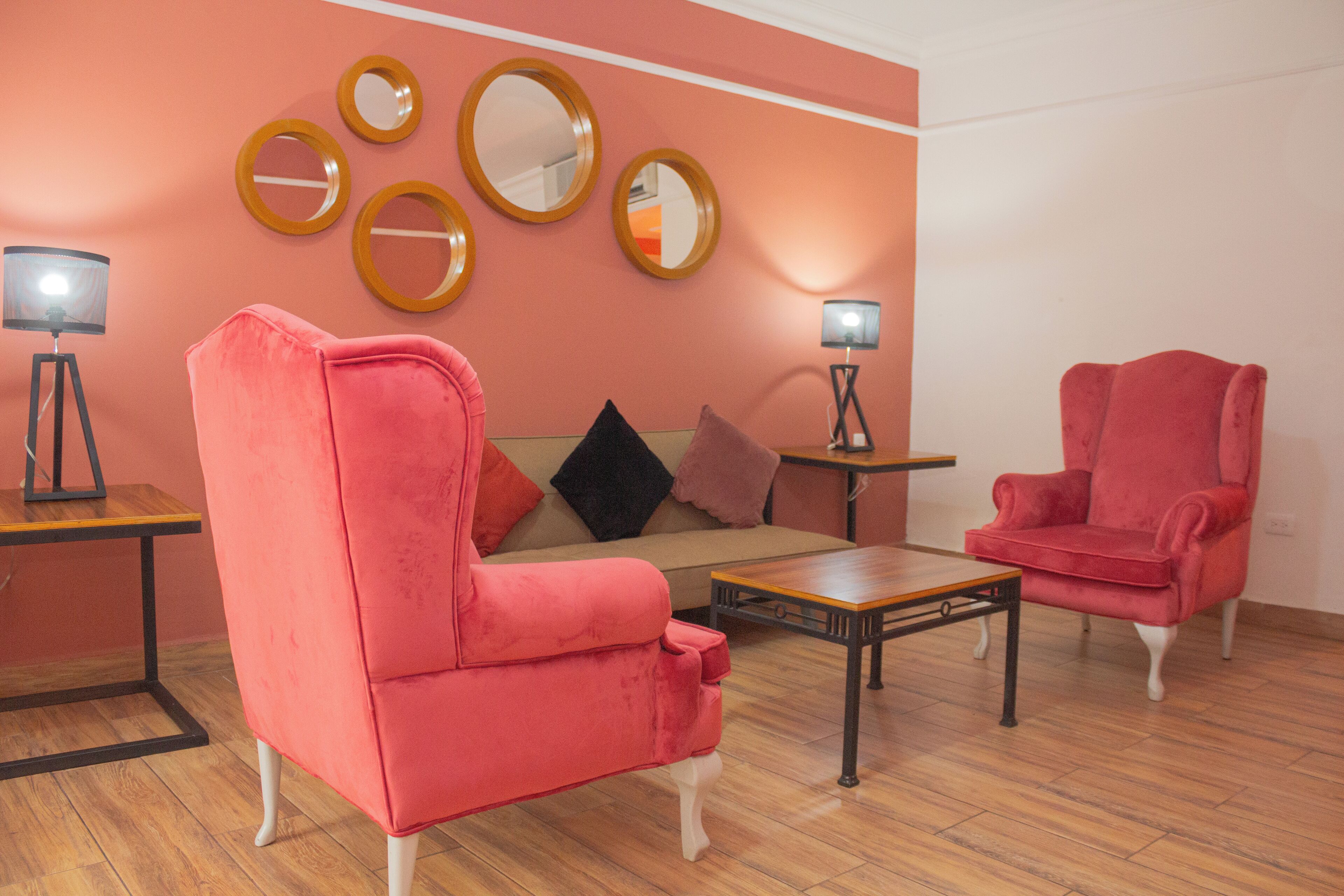 Een kamer met een roze bank, een rode fauteuil, een houten salontafel en twee vloerlampen.