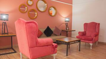 Een kamer met een roze bank, een rode fauteuil, een houten salontafel en twee vloerlampen.