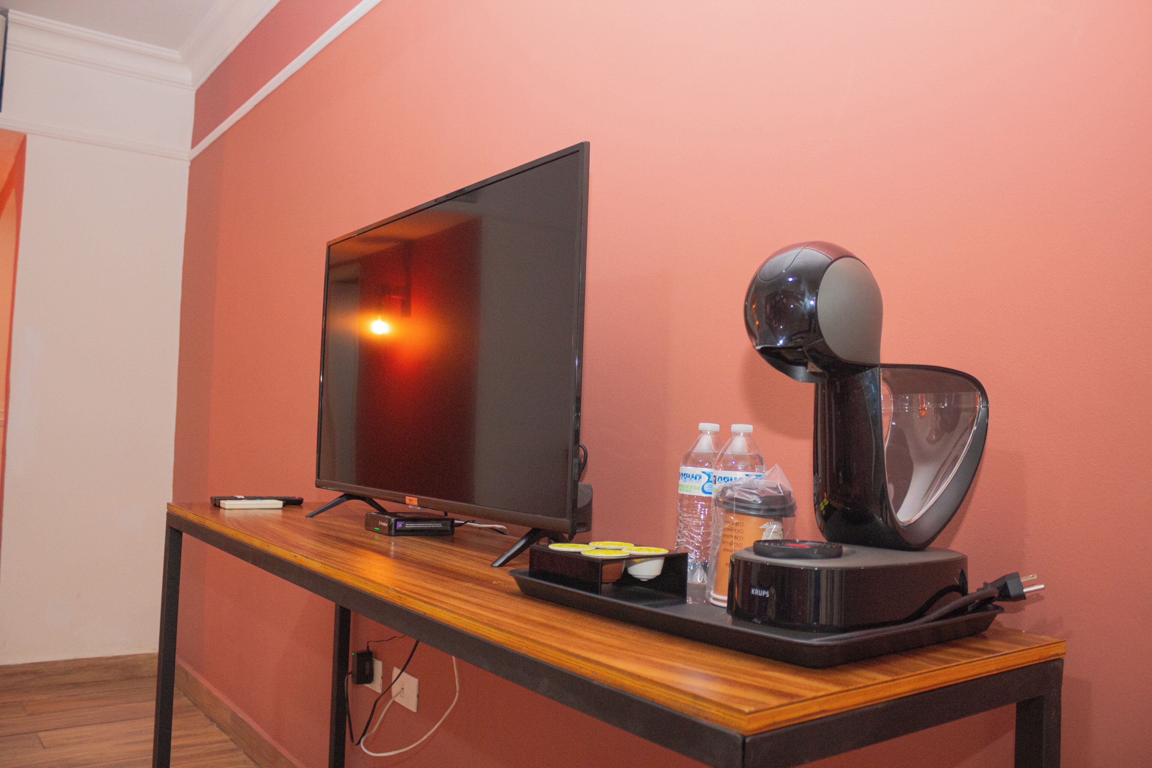 Una habitación con televisión, cafetera y agua embotellada sobre una mesa de madera.