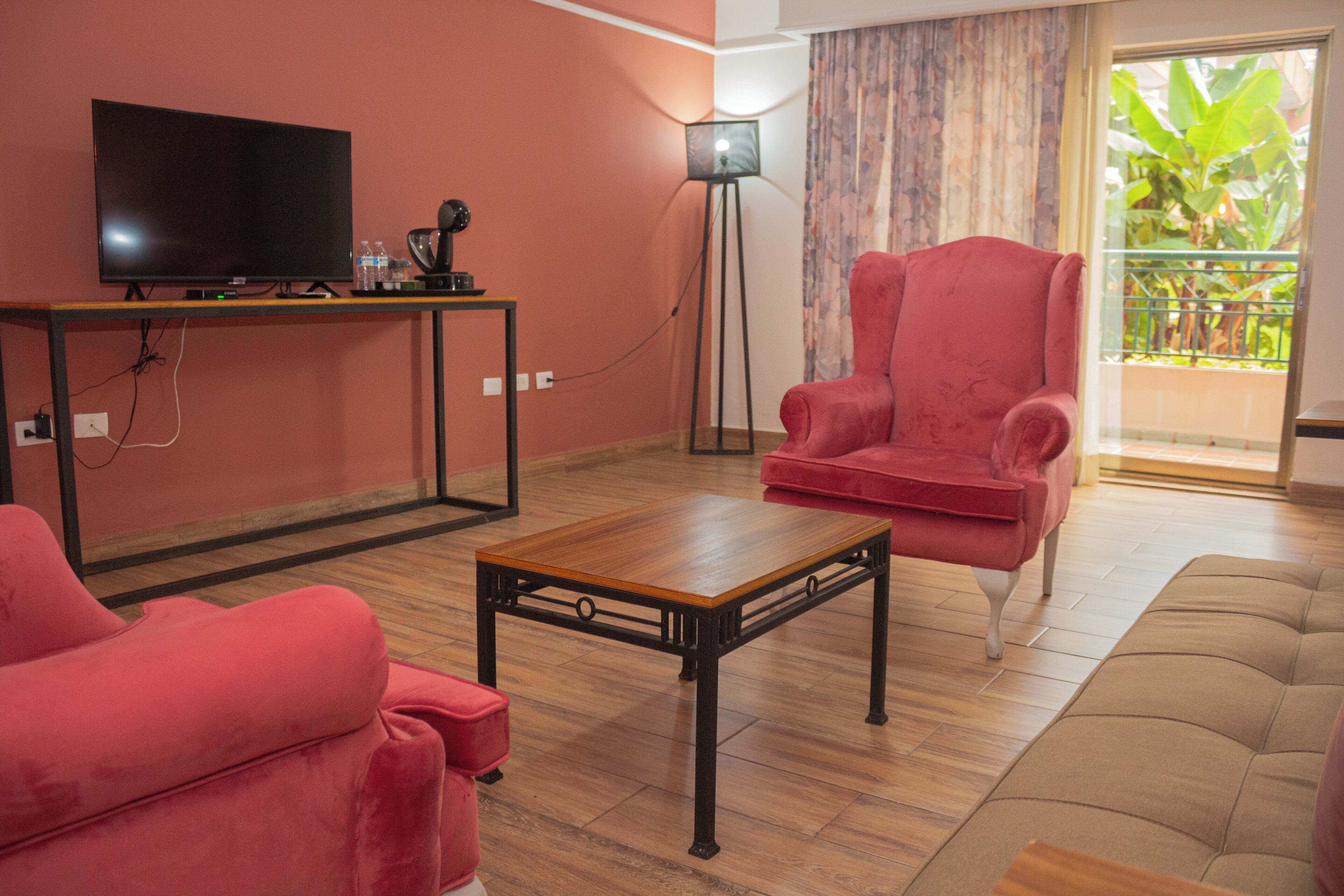 A living room with a flat-screen TV, a red armchair, a wooden coffee table, and a sofa.
