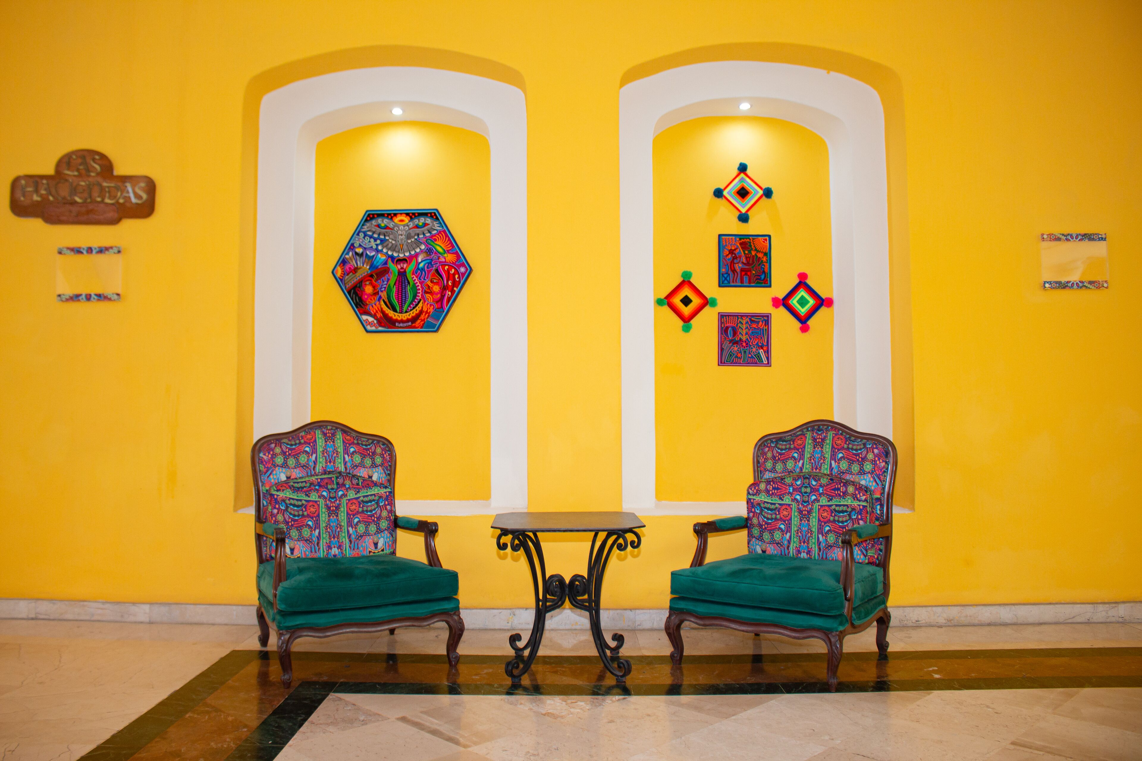 A lobby with two green upholstered chairs, a small round table, and colorful artwork on the walls.
