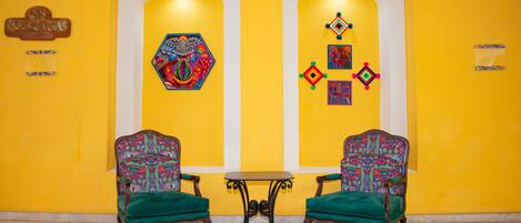 A lobby with two green upholstered chairs, a small round table, and colorful artwork on the walls.