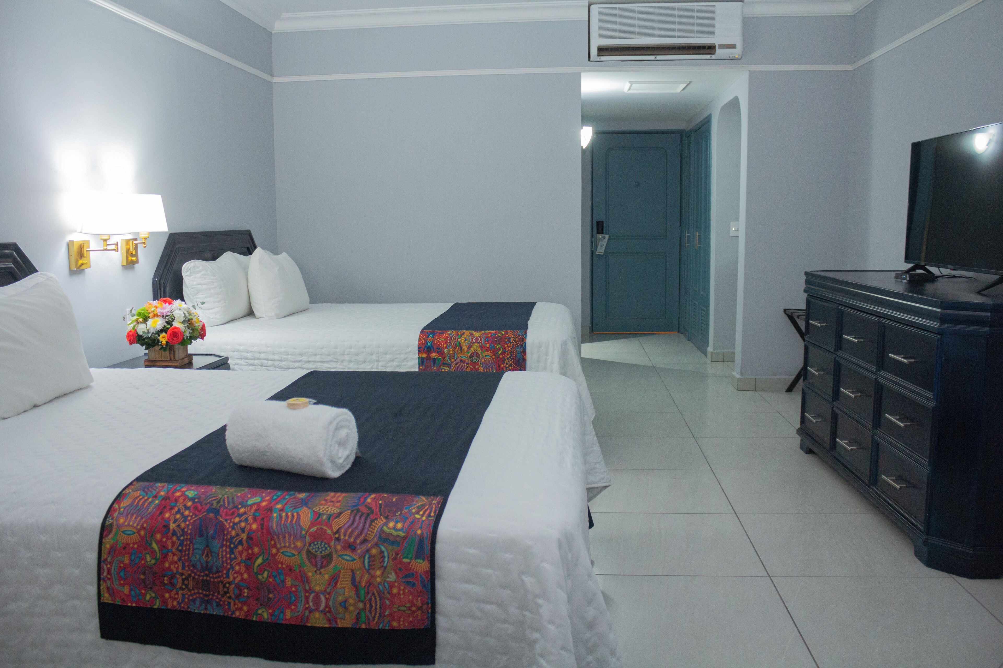 Une chambre d’hôtel avec deux lits, une télévision, une commode et une salle de bain visible au fond.