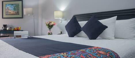 Habitación de hotel con una cama grande, una mesita de noche con lámpara, un cuadro en la pared y un jarrón con flores.
