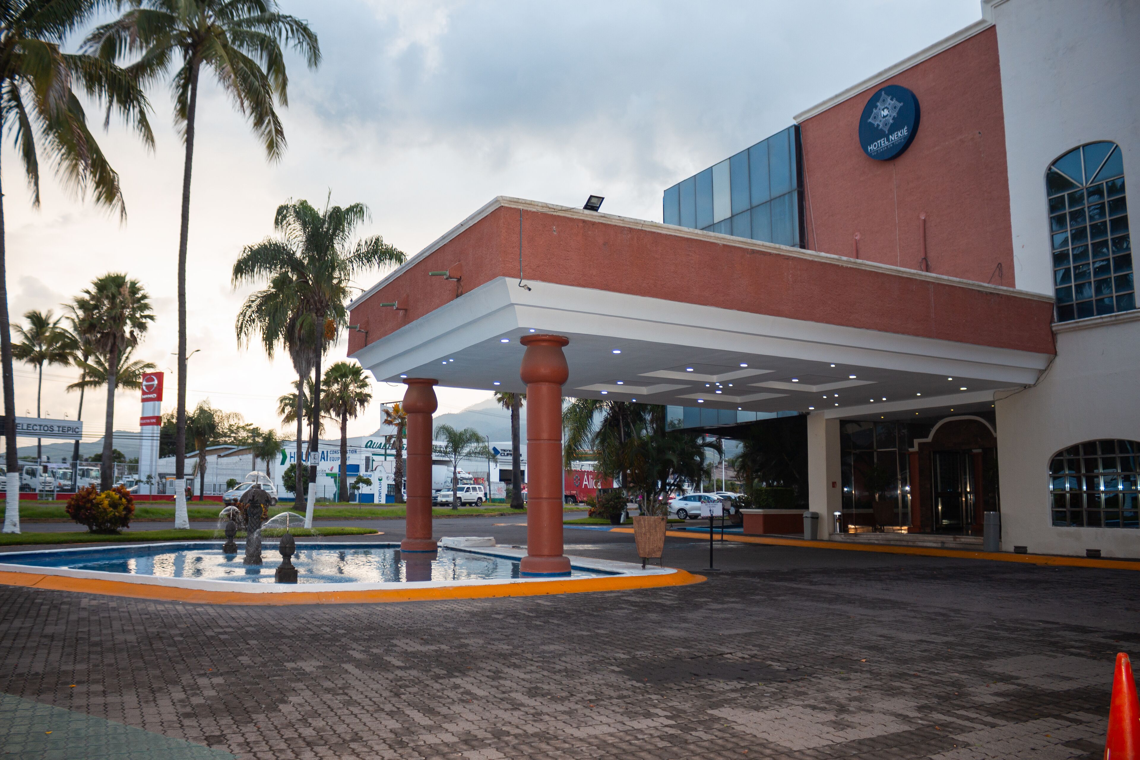 A hotel entrance with a covered walkway, palm trees, and a water feature.