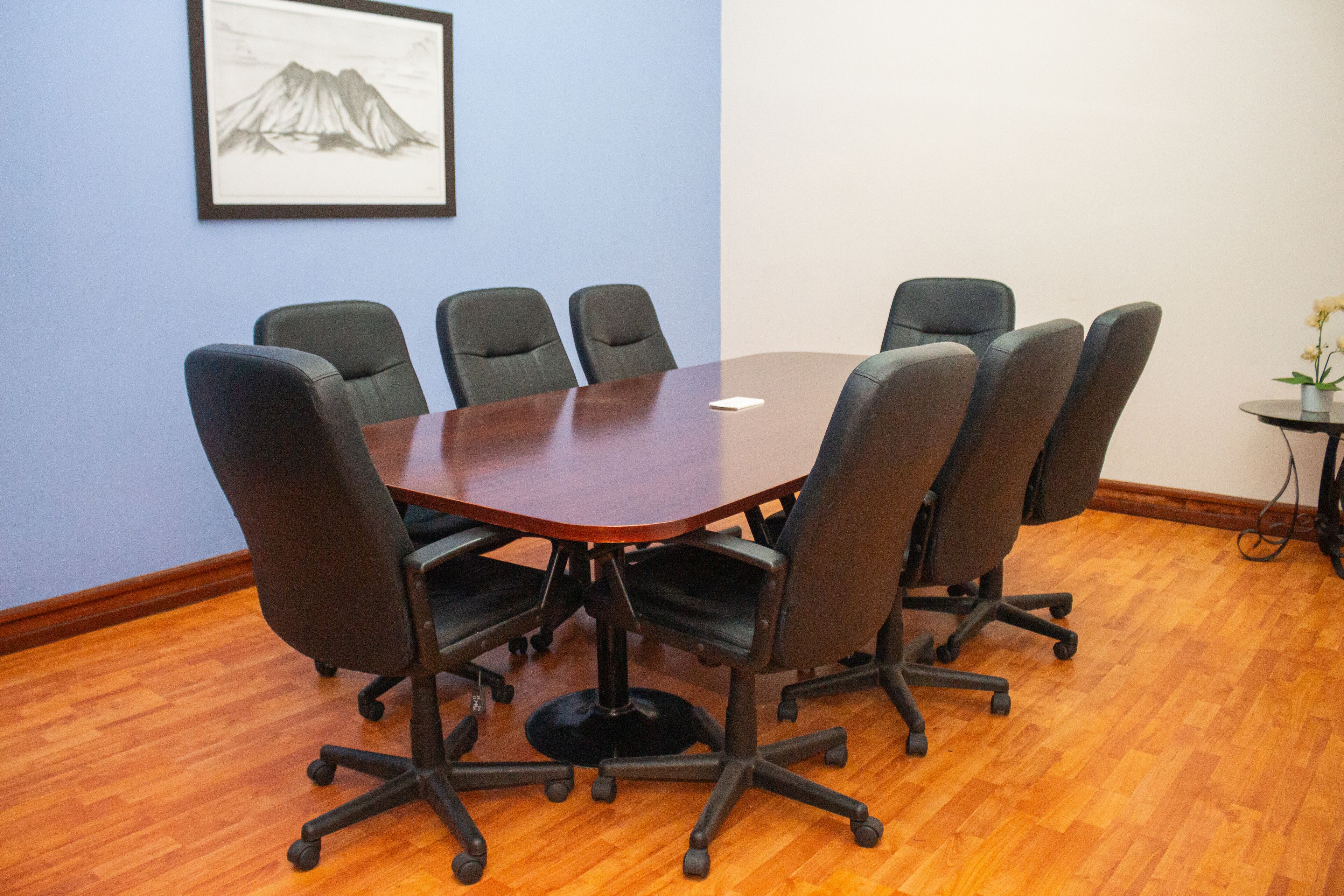A conference room with a round table, six chairs, and a framed picture on the wall.
