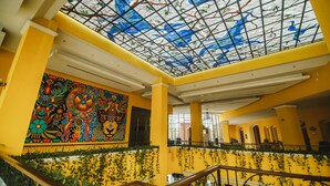 Un atrio espacioso con techo alto, un mural colorido y una escalera con barandilla.
