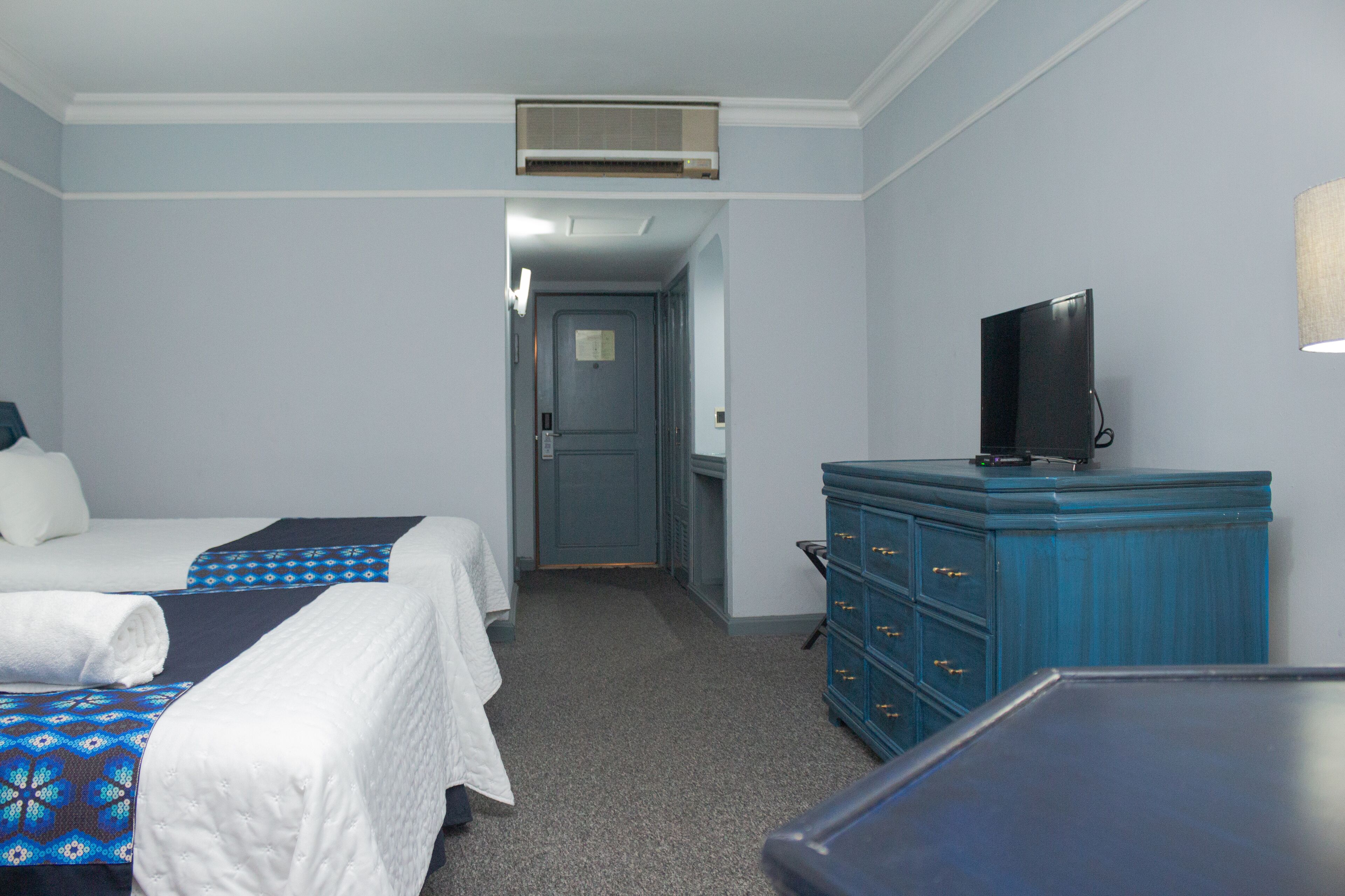 A hotel room with two beds, a dresser, a television, and an air conditioning unit.